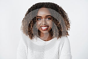 Tender and feminine happy young woman with curly haircut in winter sweater smiling satisfied and joyful gazing sincere