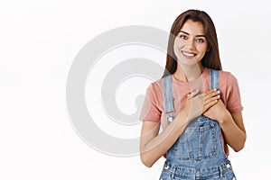 Tender, feminine lovely happy woman in overalls, t-shirt, press hands to heart, tilt head and smiling thanking dearly photo