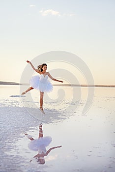 Tender girl ballerina in a white ballet dress in a graceful jump on the lake.