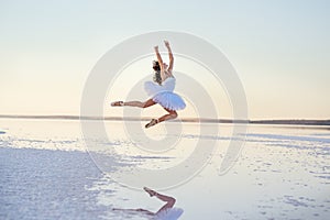 Tender girl ballerina in a white ballet dress in a graceful jump on the lake.