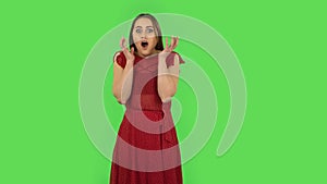 Tender girl in red dress carefully examines something then fearfully covers her face with her hand. Green screen