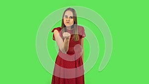 Tender girl in red dress is threatening with a fist. Green screen