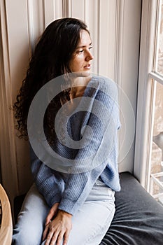 Tender girl is sitting in cafe near big window at cozy winter morning. Cheerful young woman is sitting in cozy