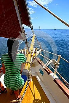 Tender girl on yacht with red sails looks ahead