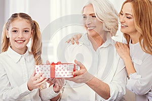 Tender granny and mother with gift congratulating radiant grandchild