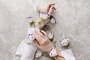 Tender hands of a girl with nude manicure on a gray grunge background with eustoma flowers. Creative illustration of hand skin