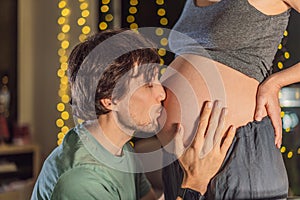 In a tender holiday moment, a husband kisses his wife& x27;s pregnant belly, expressing love and anticipation for the