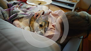 tender lovely woman dog owner lying on couch with her cute funny welsh corgi dog at cozy room. girl with pet, covered