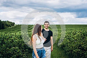 A tender loving couple walking in a field of currant. A smiling woman with long hair leads a man, holding his hand