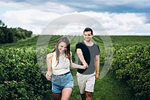 A tender loving couple walking in a field of currant. A smiling woman with long hair leads a man, holding his hand