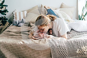 A tender mom lying on the bed hugs and kisses the baby.