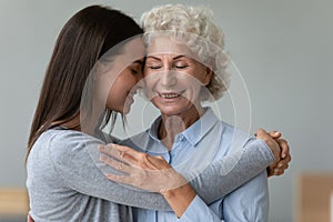 Tender moment of grownup granddaughter elderly grandmother cuddling indoors