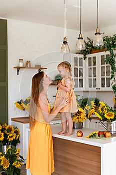 Tender mother and daughter happy together, hugging and having fun in the room full of sunflowers