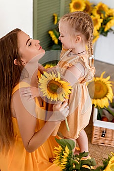 Tender mother and daughter happy together, hugging and having fun in the room full of sunflowers