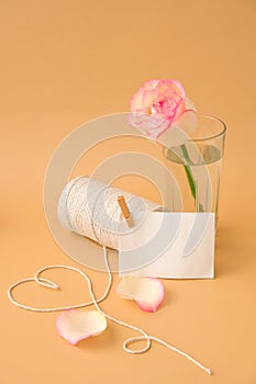 Tender pink roses with spool of white cotton rope in heart shape on beige background. Empty paper note copy space