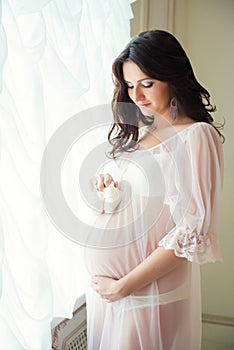 Tender pregnant mom in the subtlest peignoir holding baby booties