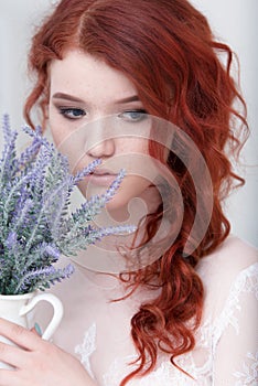 Tender retro portrait of a young beautiful dreamy redhead woman in beautiful white dress with bouquet of lavender.