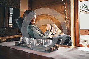 Tender scene with woman and her beagle dog in comfortable chair opposite big window in cozy country home. Countryside vacation