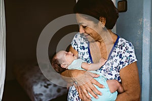 Tender scene of young grandmother holding granddaughter with natural light at home smiling. Intimate moment