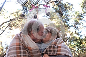 A tender senior couple exchanges a kiss under the blanket outside in the woods. Love and freedom concept