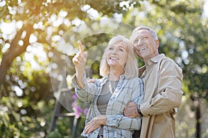 Tender senior spouses walking in their garden, enjoying warm spring day outdoors, embracing and looking away