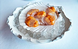 Tender slices of scallop covered with orange pike caviar on white mollusc shell in ice pieces