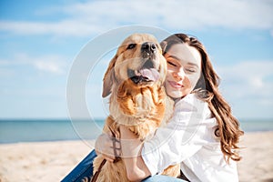 Tender smiling young woman hugging her dog on the beach