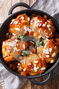 Tender sticky chicken thighs with apricot glaze and almond flakes close-up in a pan. Vertical top view