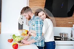 Tender woman hugging her husband while he cutting vegetables