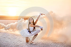 Tender young ballerina dancer in a snow-white tutu dress and white pointe shoes in pink smoke.  on a salty dried lake. Fantastic l