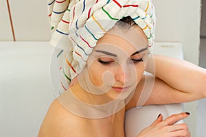 Tender young girl with towel on the hair lies in the bathroom and looks down