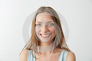 Tender young pretty girl looking at camera smiling listening to streaming music in headphones over white background.
