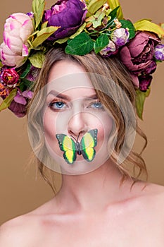 Tender young woman posing in flower wreath with artificial  greenbutterfly,  isolated on ochet background. butterfly covering