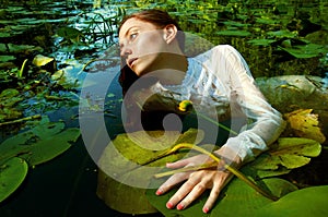 Tender young woman swimming in the pond among water lilies