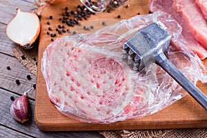 Tenderization of fresh pork steak on wooden chopping board