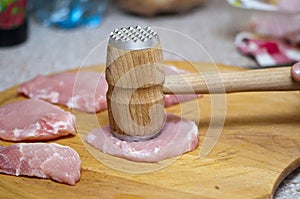 Tenderize slabs of meat on wooden board