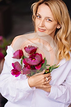 tenderness. a blonde woman in a white shirt and a bouquet of peonies.