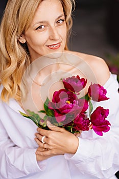 tenderness. a blonde woman in a white shirt and a bouquet of peonies.