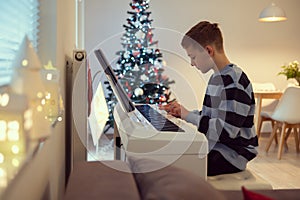 Tennage boy practise plaing piano with new years tree on background