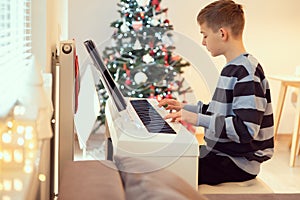 Tennage boy practise plaing piano with new years tree on background