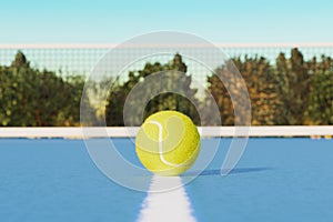 Tennis ball on the court line against the background of a sports court net.