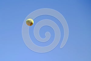 tennis ball frozen midair during serve, with clear blue sky backdrop