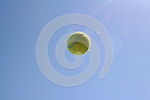 tennis ball frozen midair during serve, with clear blue sky backdrop