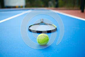 Tennis ball is laying in front of racket on opened tennis cort.