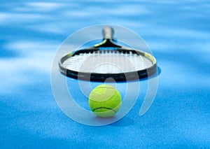 Tennis ball is laying near racket on blue cort carpet. photo