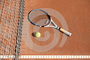 Tennis ball and racket on the ground on a clay tennis court next to the net and line