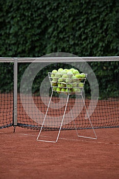 Tennis balls in basket is near the net. Selective focus, design element. Clay tennis court outdoors. Sport game, Leisure activity