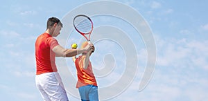 Tennis coach or instructor and child tennis player. Kids tennis on the court. Blue sky background. Banner Copy space