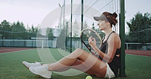 On the tennis court a sportiv woman prepare for a tennis game , sitting on the floor and relaxing.