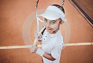 Tennis is my favorite game! Portrait of a pretty sporty child with a tennis racket. Little girl smiling at camera on tennis court